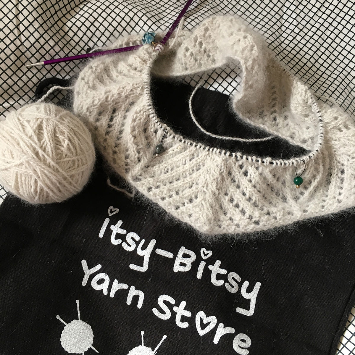 Lace and cabled qiviut cowl with a couple of inches done, on a project bag that reads, "Itsy-Bitsy Yarn Store".