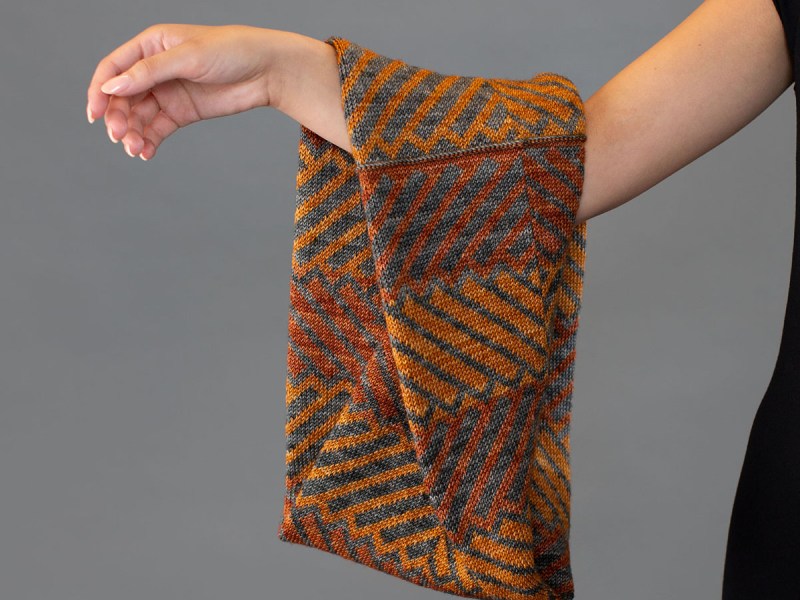 Hand knit colourwork cowl hanging from a woman's arm.