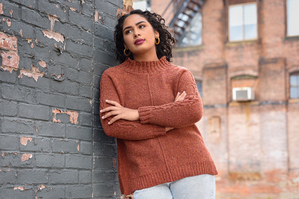 A woman wearing a hand knit pullover, viewed from the front.