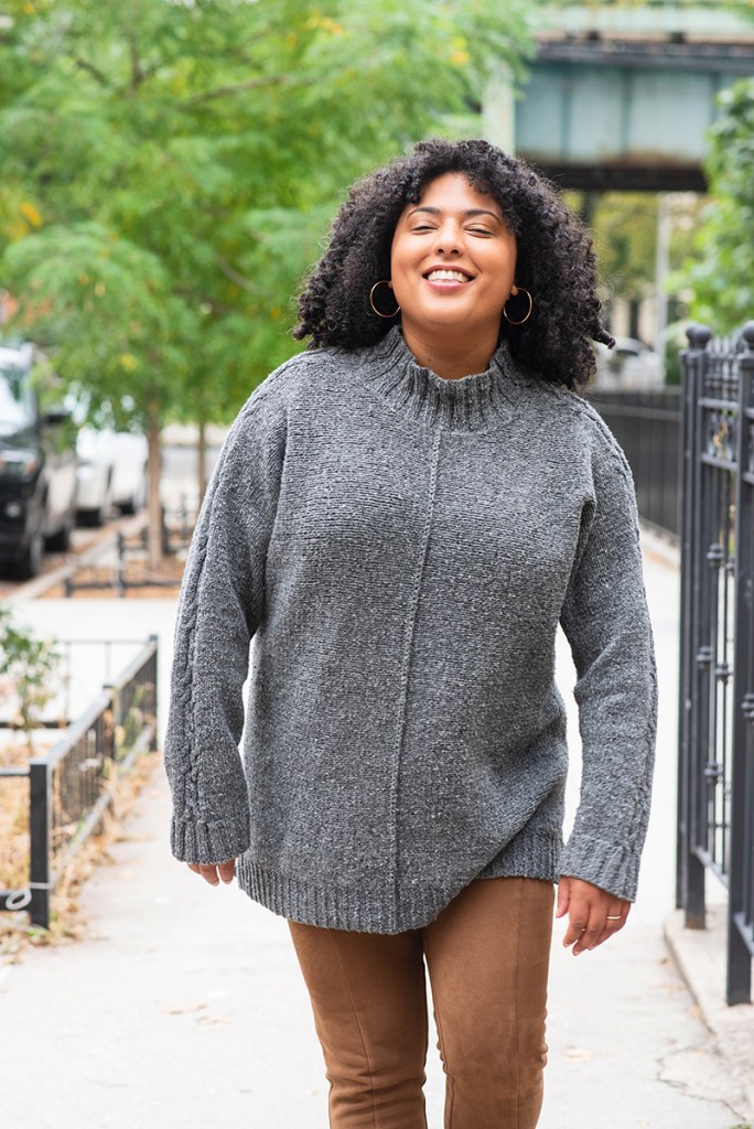Front view of a woman walking, wearing a hand knit pullover.