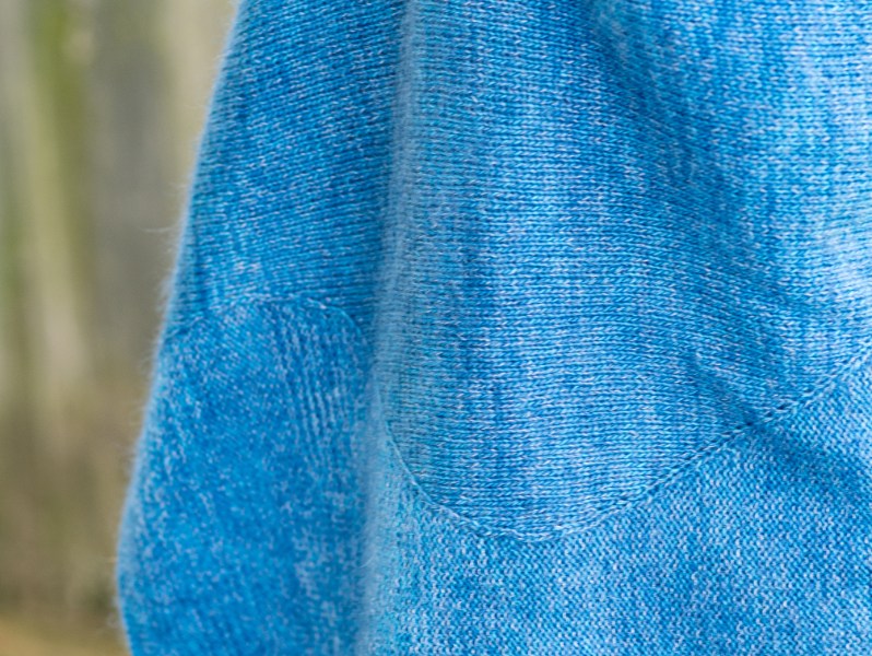 Close up of a hand knit blue shawl with sections of stockinette and reverse stockinette separated by a long, wavy line.