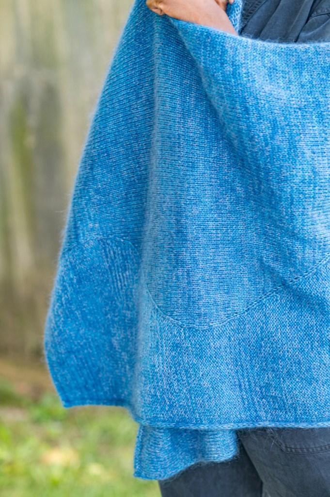 Close up of a hand knit blue shawl with sections of stockinette and reverse stockinette separated by a long, wavy line.