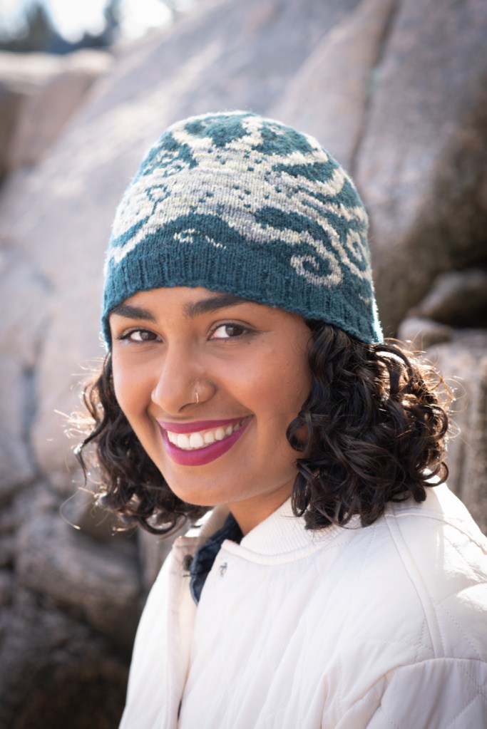 A smiling woman wearing the Enter Octopus hat, showing the front of the hat with the body and part of the head of an octopus.