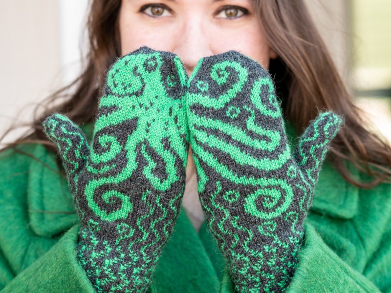 A woman holding her hands in front of her face with their backs to the camera. The octopus on her mittens flows across both hands.
