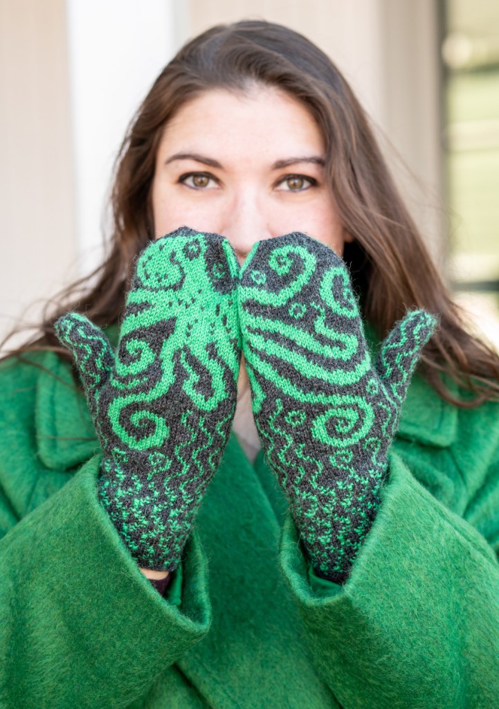 A woman holding her hands in front of her face with their backs to the camera. The octopus on her mittens flows across both hands.