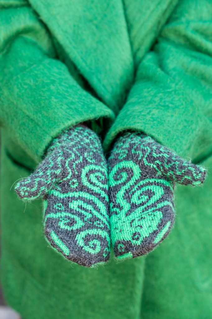 Two hands held out to the camera side by side, palms facing up, fingers towards the camera. The octopus on her handknit mittens flows across both hands.